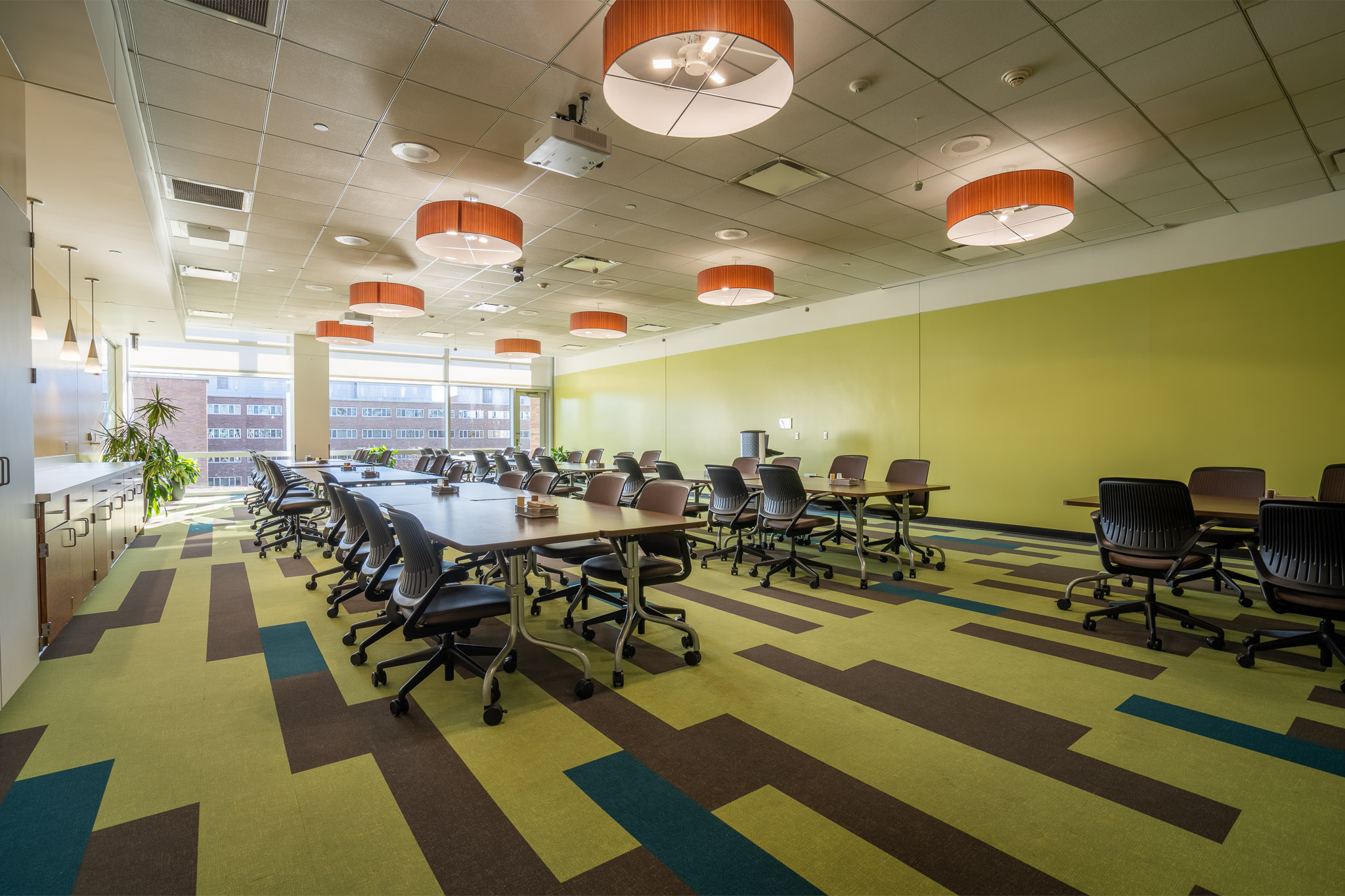 Spacious conference room with tables, mesh chairs, orange lights, and geometric carpet.