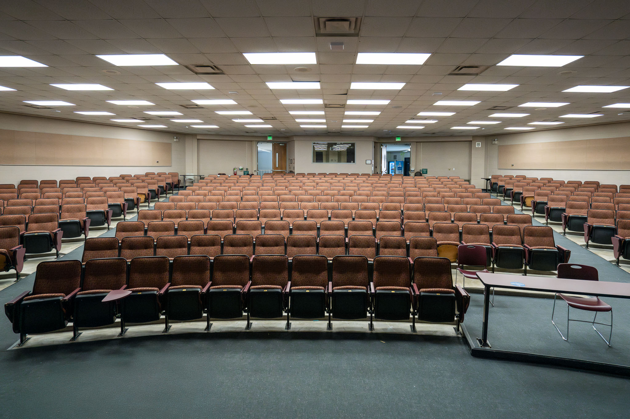 Empty lecture hall with tiered brown seating and overhead fluorescent lighting.
