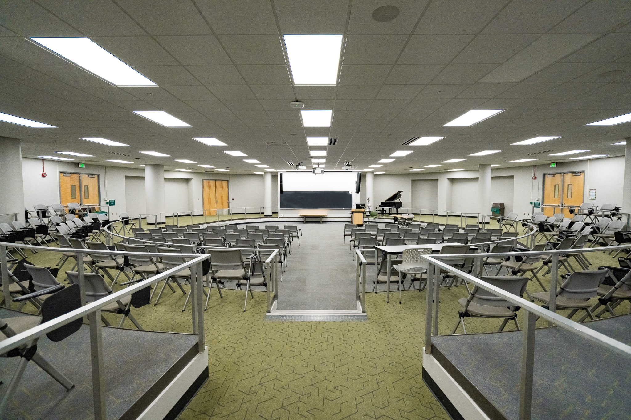 Circular university lecture hall with tiered blue seating and beige ceiling fixtures.