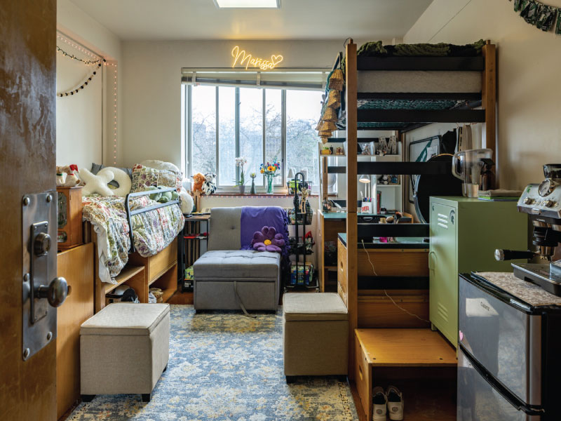 A neat dorm room with two lofted beds, desks underneath, and a central window with string lights.