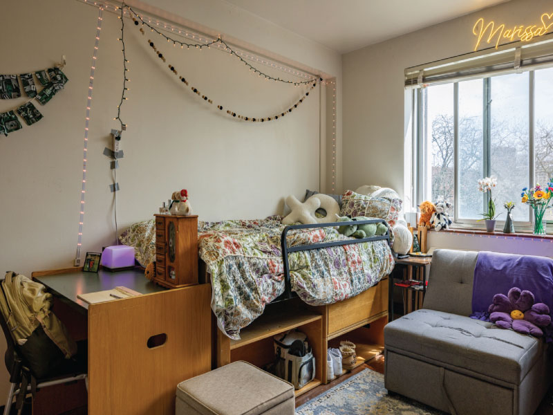 A neat dorm room with two lofted beds, desks underneath, and a central window with string lights.