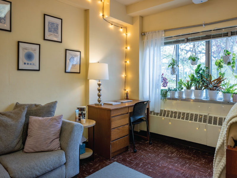 Neatly organized dorm room with one bed a desk with a lamp.