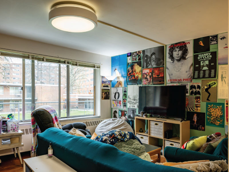 A living room with a teal sofa, large window, and walls covered in posters.