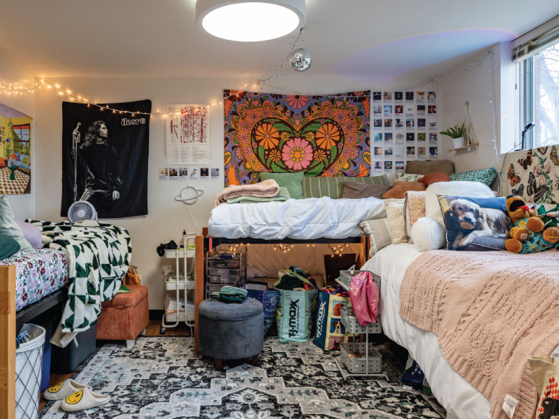 A colorful college dorm room with three lofted beds, decorative lights, a heart tapestry, and personal items.