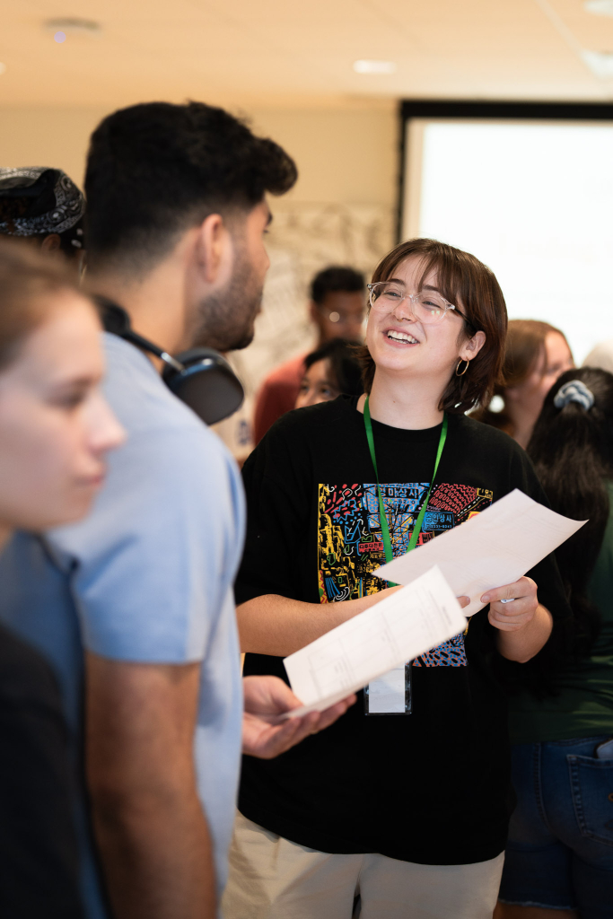 Undergraduate students talking, one is smiling and holding a piece of paper in their hands.