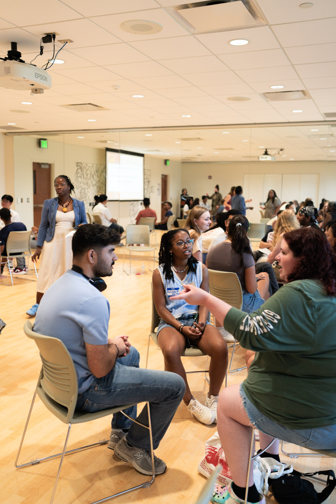 Undergraduate students sitting and facing each other while in discussion. One student is making hand motions as they explain something.