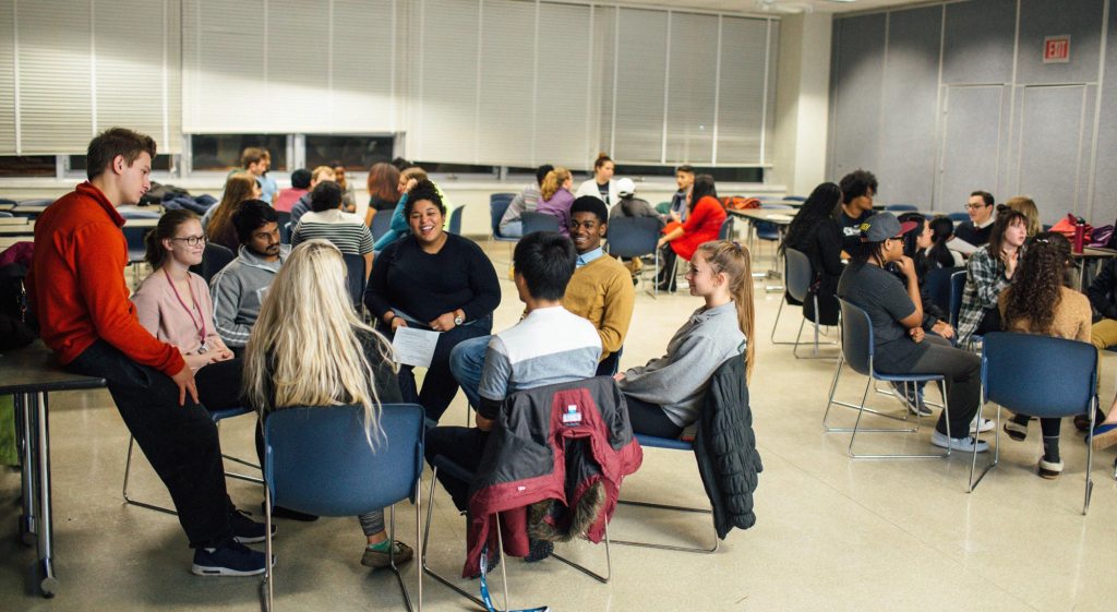 Students gathered in circle-shared groups, looking at each other as they hold conversation.